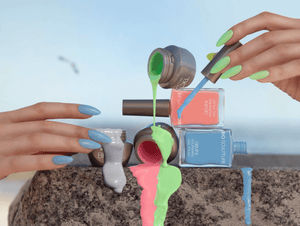 A close-up of a person's hands with painted nails holding BIOGEL and GEMINI'S Delice Pastel" nail polish and gel colors 